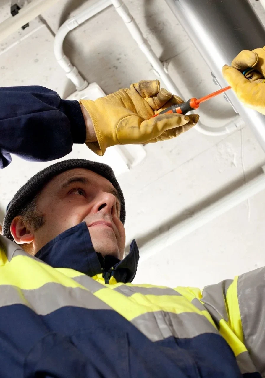 A man in yellow and blue jacket holding an orange wire.